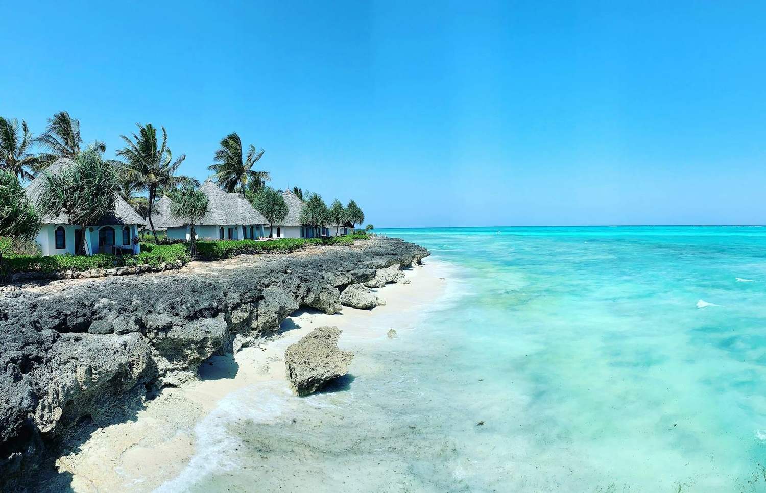 A turquoise Zanzibar coastline with thatched bungalows on a coral shore