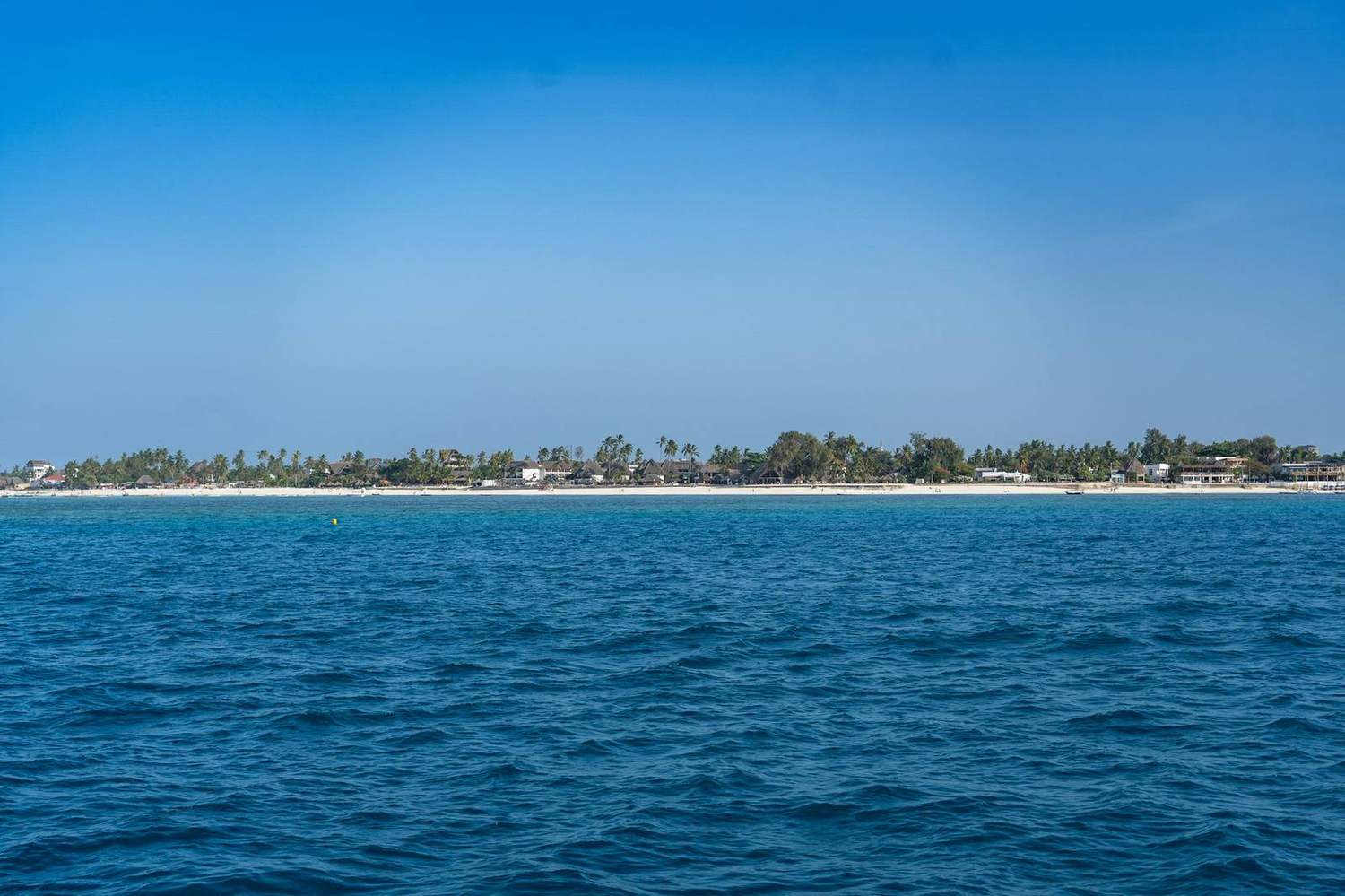 A white-sand beach and turquoise sea seen from a boat off Zanzibar